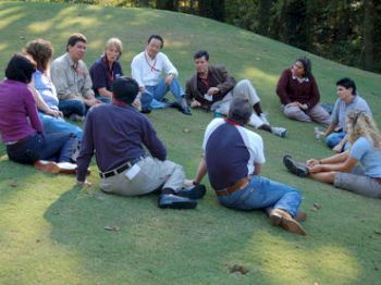 A group of people sitting in a circle on a grassy field, seemingly engaged in a discussion or meeting outdoors.