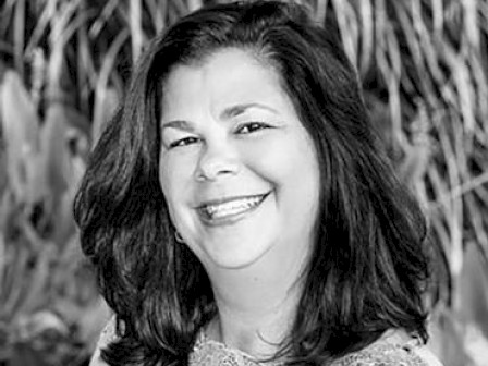 A woman is smiling in a black-and-white photo against a blurred natural background.