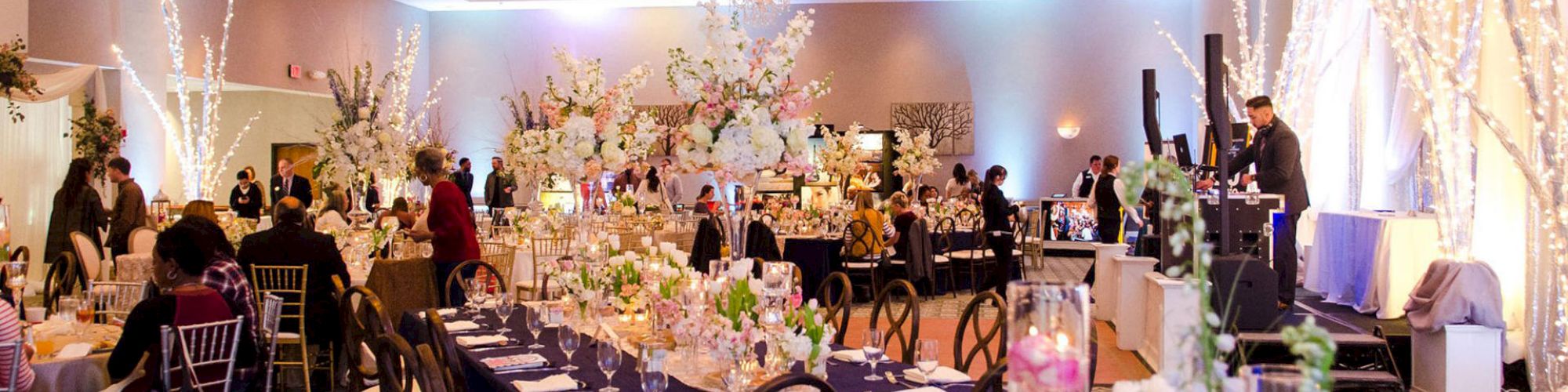 A beautifully decorated banquet hall set for an event, featuring elegant floral arrangements, candlelit tables, and guests enjoying the ambiance.