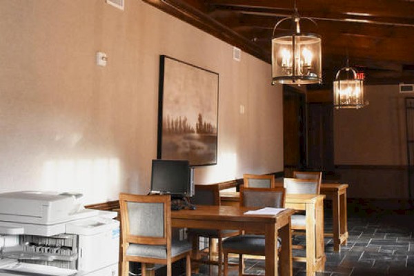 The image shows a small office area with a printer, several wooden desks and chairs, a computer, and framed artwork on the wall, illuminated by lanterns.