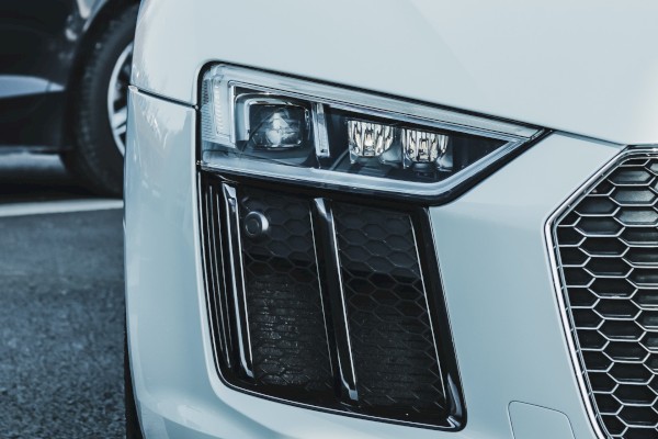 The image shows the front view of a white sports car, parked closely to another vehicle, showcasing its headlight and grille.