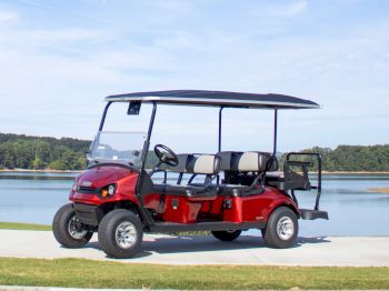 A red golf cart with a black roof is parked on a path by a lake with trees in the background.