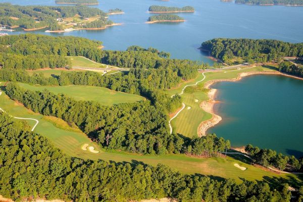 The image shows an aerial view of a scenic golf course surrounded by lush trees and water bodies, with winding paths and several golf holes visible.