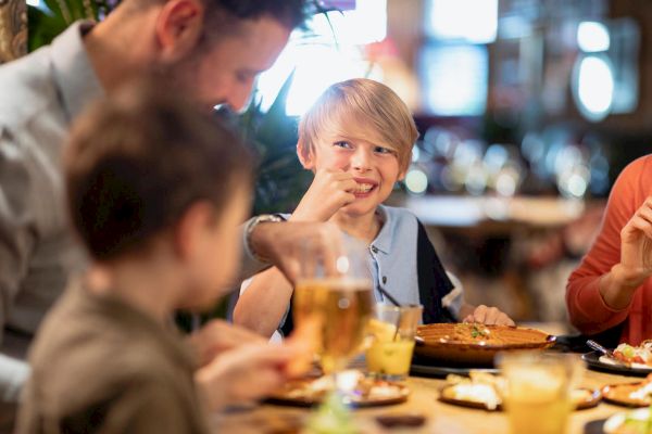 A family is enjoying a meal together at a restaurant, with the children happily eating and the adults engaging in conversation over the food.