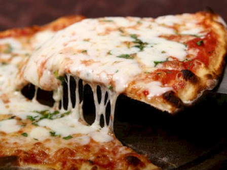 A close-up of a cheesy pizza slice being pulled away from the rest of the pizza, with melted cheese stretching.