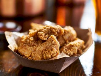 A basket filled with crispy, golden-brown fried chicken pieces is set on a wooden table.