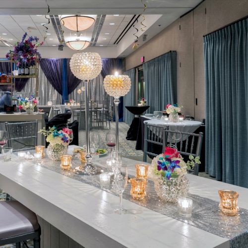 A decorated reception area with a modern, elegant setting, featuring floral arrangements, candles, glass decor, and dim lighting.
