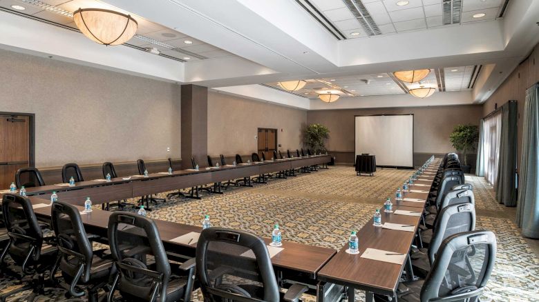 A large conference room with tables arranged in a U-shape, equipped with chairs, water bottles, and notepads, ready for a meeting or presentation.