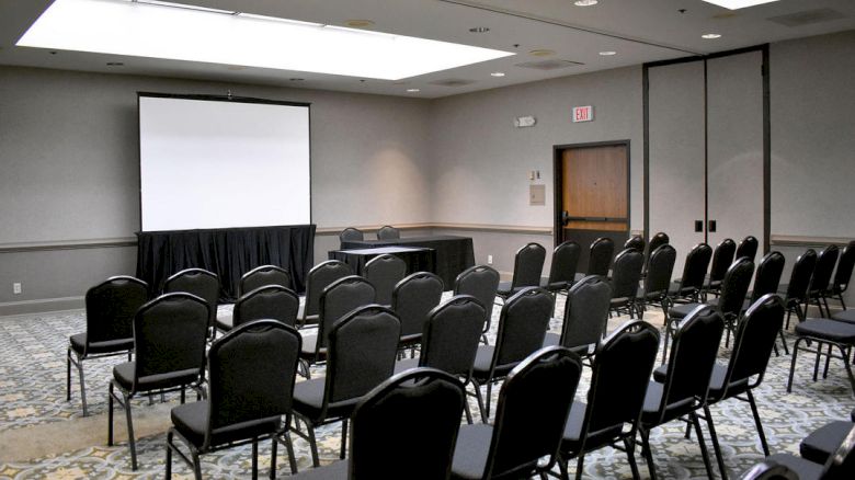 This image shows a conference room with rows of empty chairs facing a screen and projector, ready for a presentation or meeting.