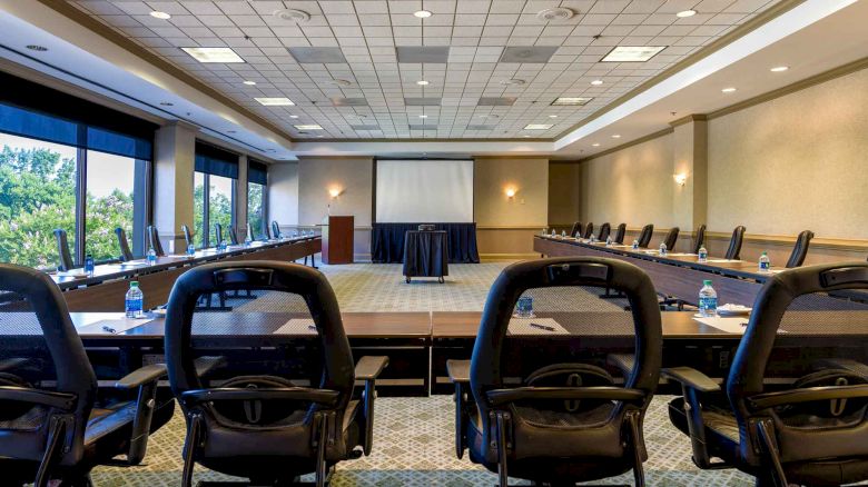 A large conference room with office chairs, tables, a projector screen, and water bottles placed on the tables, set up for a meeting or presentation.