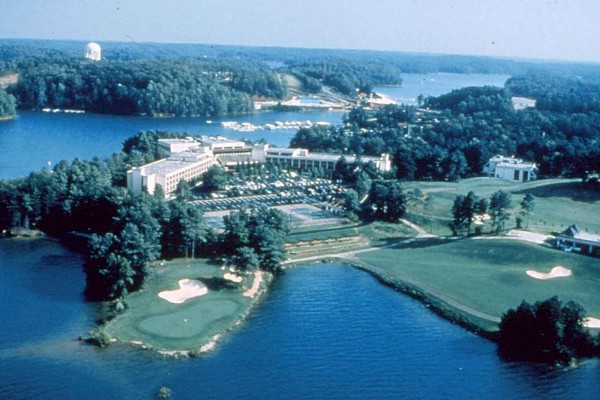 The image shows an aerial view of a lakeside resort complex with a golf course, numerous buildings, and surrounding forested areas, ending the sentence.