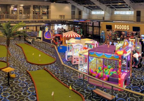 This image shows an indoor entertainment venue with arcade games, mini-golf courses, a small carousel, and a snack bar in the background.