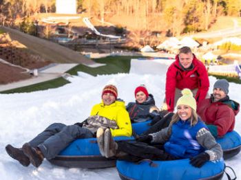 A group of people is enjoying snow tubing on a sunny day at a winter resort, smiling at the camera and seated in blue inflatable tubes.