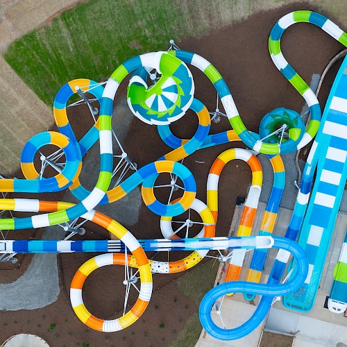 An aerial view of a colorful water park with multiple winding slides, including tubes and open slides, and green and blue elements, seen from above.