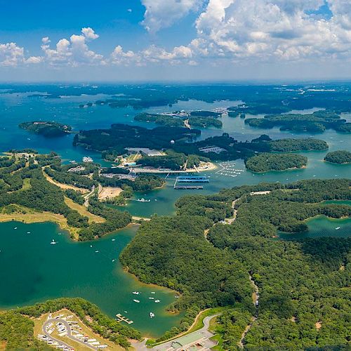 This image shows an aerial view of a lake featuring many small islands, boats, and surrounding greenery under a partly cloudy sky.