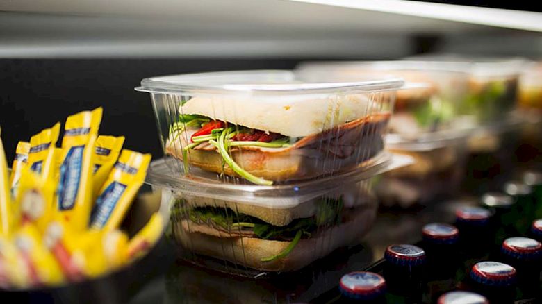 Stacks of packaged sandwiches are in a display case, accompanied by yellow condiment packets and bottles with red caps.