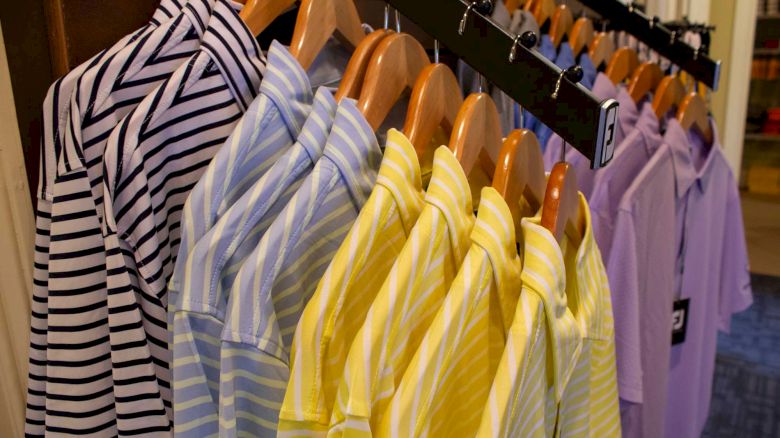 A rack of striped shirts in various colors, including black and white, blue, yellow, and purple, displayed on wooden hangers in a store.
