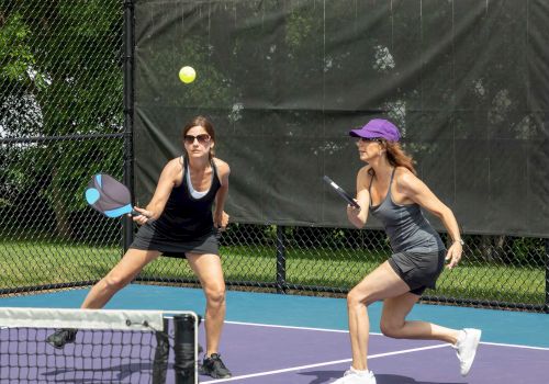 Two women are playing pickleball on an outdoor court, both focused on an incoming ball.