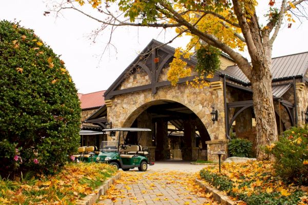 A rustic stone building with a wooden archway, surrounded by autumn leaves and a golf cart parked out front.