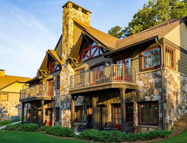 This image shows a charming, rustic-style house with stone and wood details, featuring balconies and surrounded by greenery.