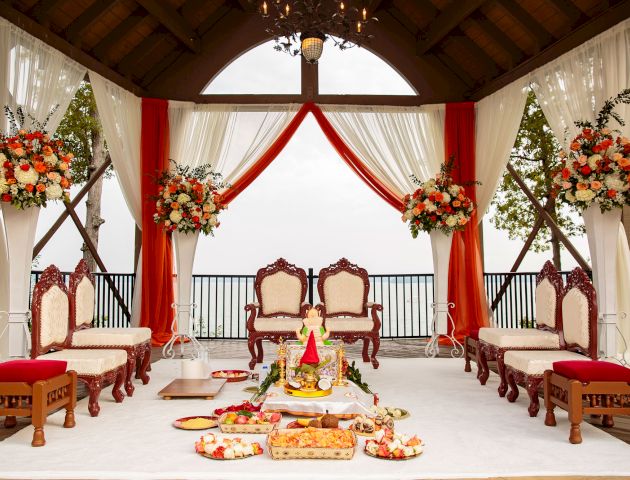 A beautifully decorated gazebo features elegant chairs, vibrant floral arrangements, and traditional items set up for a ceremonial event.