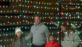 A family of four is enjoying a night out surrounded by festive holiday lights, with two children and two adults smiling and interacting with each other.