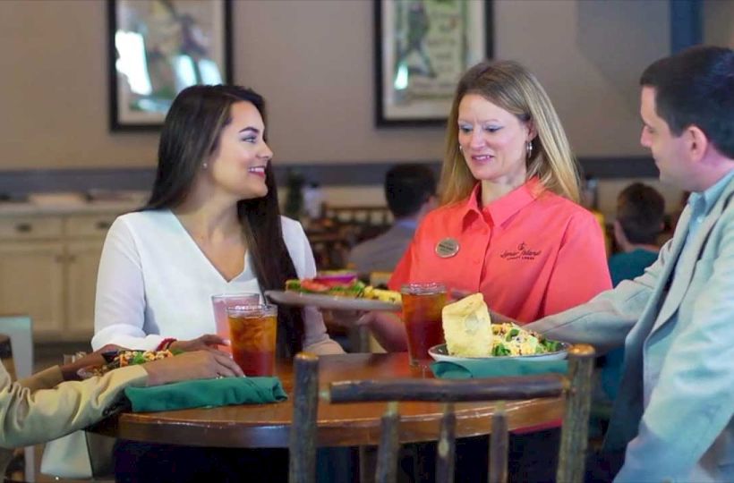A group of three people at a restaurant conversing as a waitress serves their food and drinks.