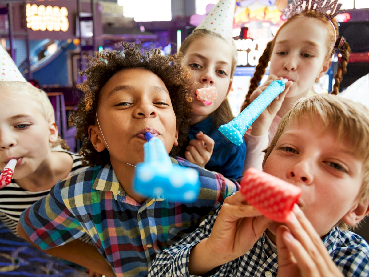 A group of children are wearing party hats and blowing party blowers, appearing to enjoy a festive celebration.