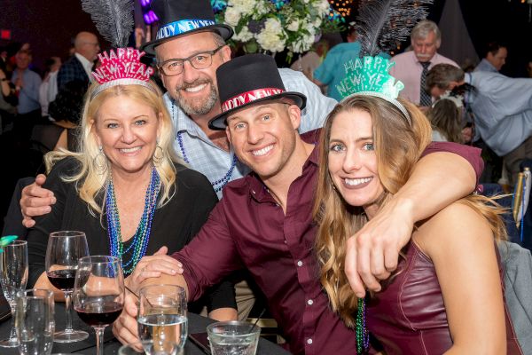 Four people enjoying a New Year's celebration, wearing hats that say 