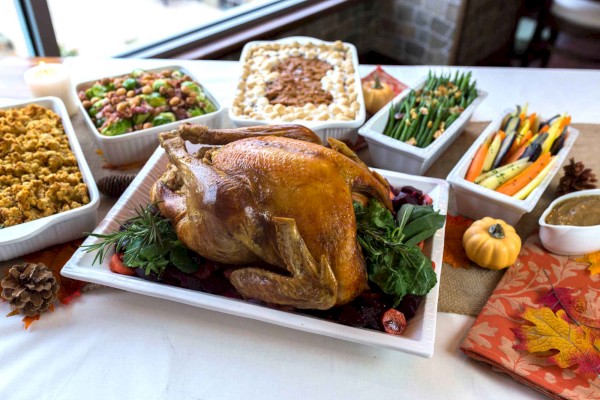 A roasted turkey is surrounded by various side dishes including stuffing, Brussels sprouts, green beans, mashed potatoes, and glazed carrots.