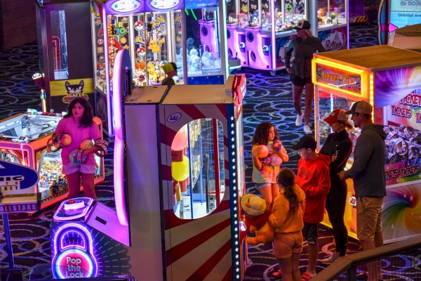 People are playing various arcade games in a vibrant, brightly lit game room filled with claw machines and other gaming equipment.