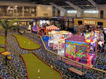 An indoor amusement center featuring mini golf, arcade games, claw machines, and a shop called 