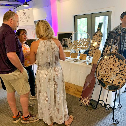 Several people gather around a display table with decorative items and crafts in a well-lit indoor setting.