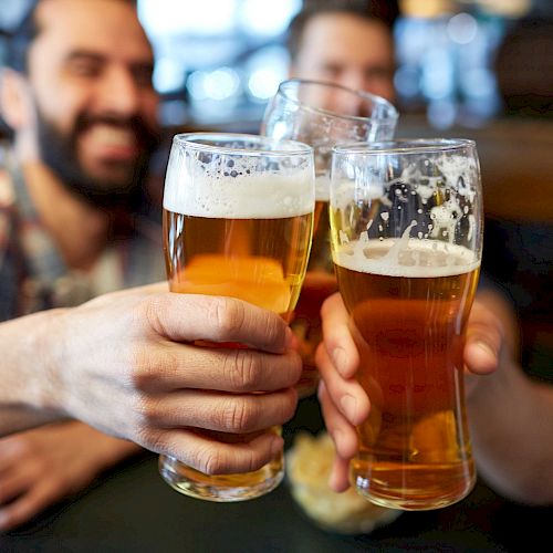 Three people clinking glasses of beer in a toast at a bar, smiling and enjoying their drinks.