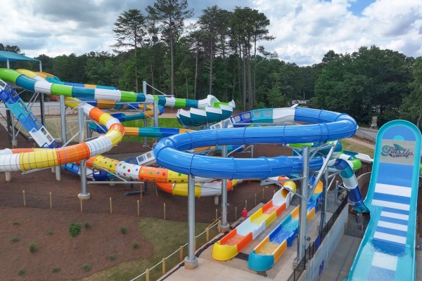 The image shows a colorful water park with multiple water slides and greenery in the background.
