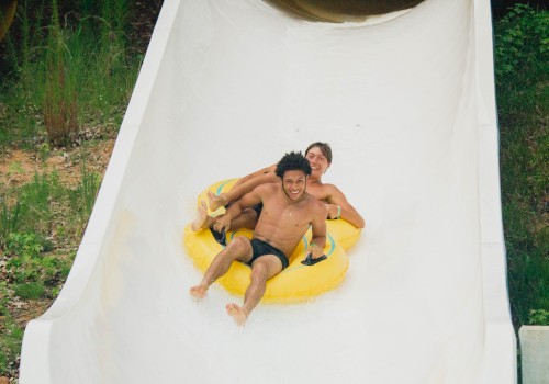 Two people riding down a white water slide on a yellow inflatable raft, smiling and enjoying the experience.