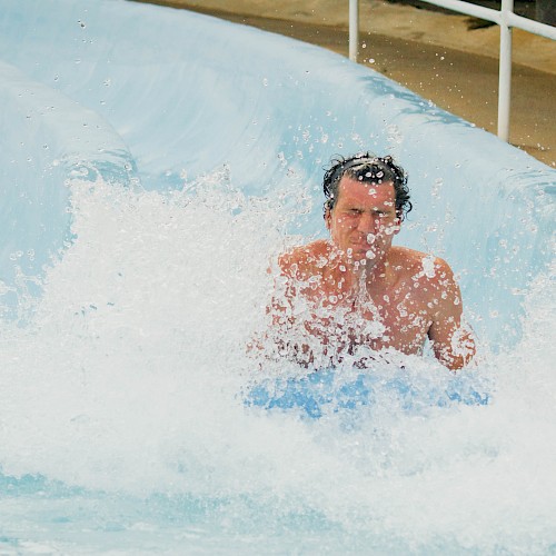 A person is riding a water slide, splashing into the pool below, creating a large splash and appearing to have fun.