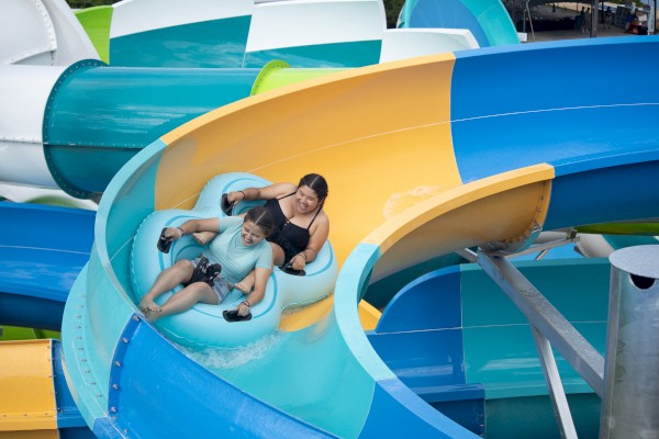 Two people are enjoying a ride on a colorful water slide, sitting in a blue inflatable tube.