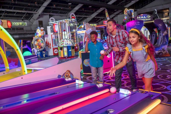 A group of people having fun playing skee-ball in an arcade filled with colorful games and lights.