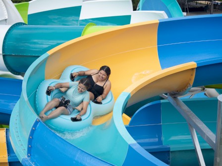Two people are enjoying a ride on an inflatable tube slide at a water park, surrounded by colorful tubes and structures.