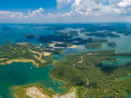 The image shows an aerial view of a lake with numerous small islands, marinas, and boats, surrounded by lush green landscapes under a partly cloudy sky.