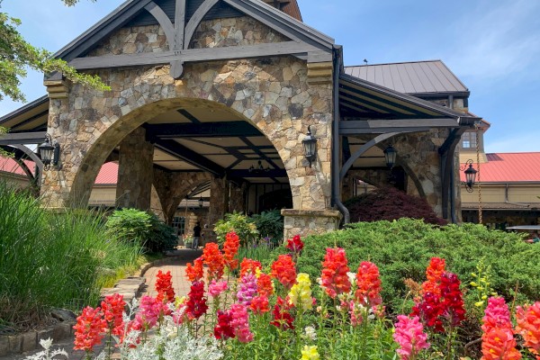 The image shows a stone building with a large archway, surrounded by colorful flowers and greenery. It appears to be a scenic area.