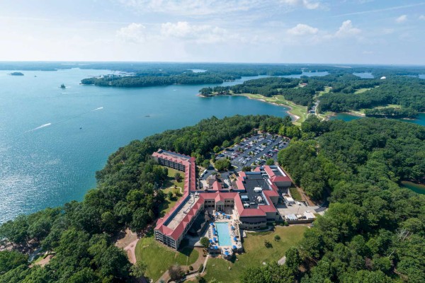 Aerial view of a large resort surrounded by dense trees and situated near a body of water with some boats visible.