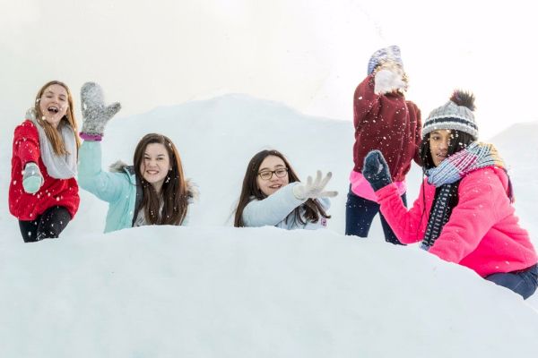 Five people standing in the snow, smiling, and wearing winter clothing; they appear to be playing and having fun.