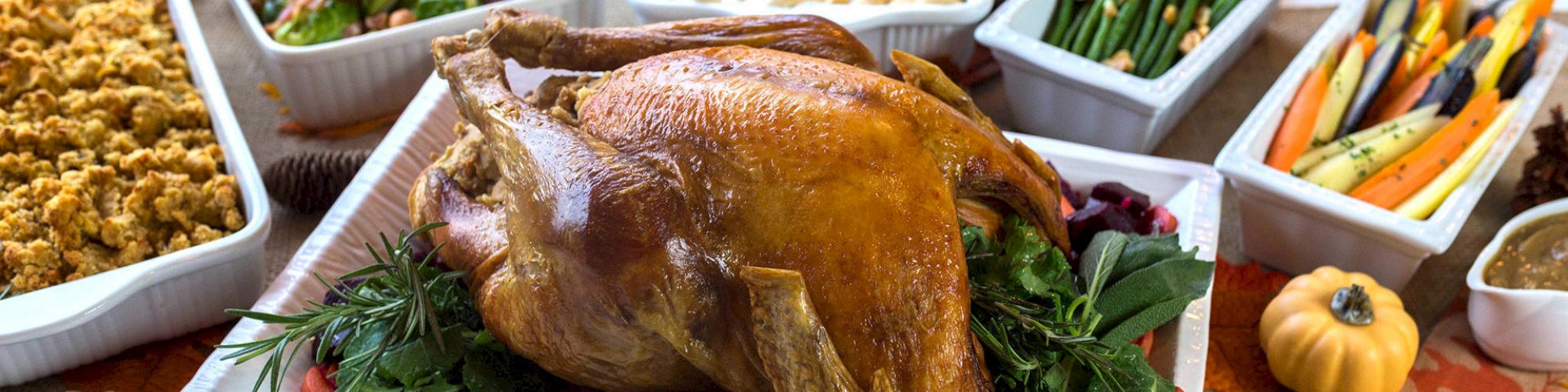 A roasted turkey is surrounded by side dishes including green beans, carrots, mashed sweet potatoes, stuffing, and mixed vegetables.