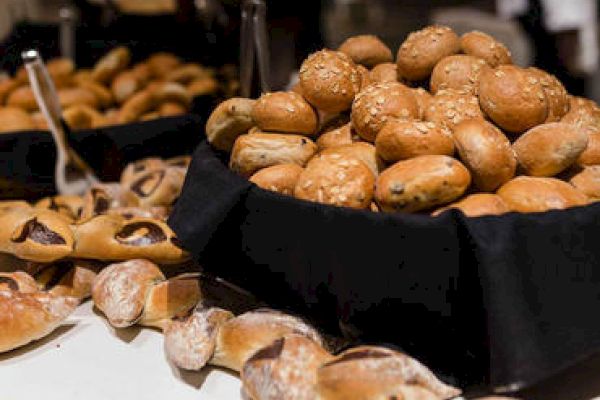 An assortmAn assortment of bread rolls and pastries arranged in baskets and on a table, likely at a buffet or bakery setting.