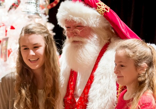 Two young girls are posing with a man dressed as Santa Claus in front of a festive Christmas tree, all smiling happily.