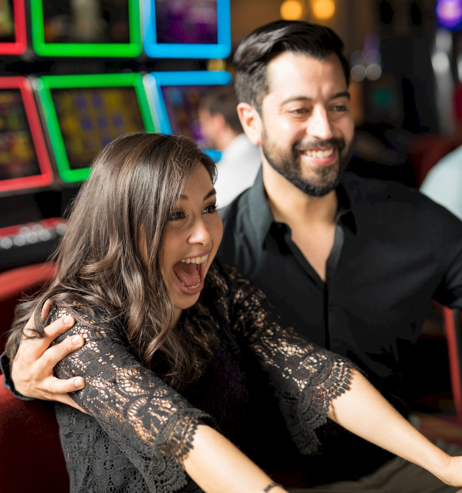 A man and woman are celebrating while playing on slot machines in a casino, with a joyful and excited expression.