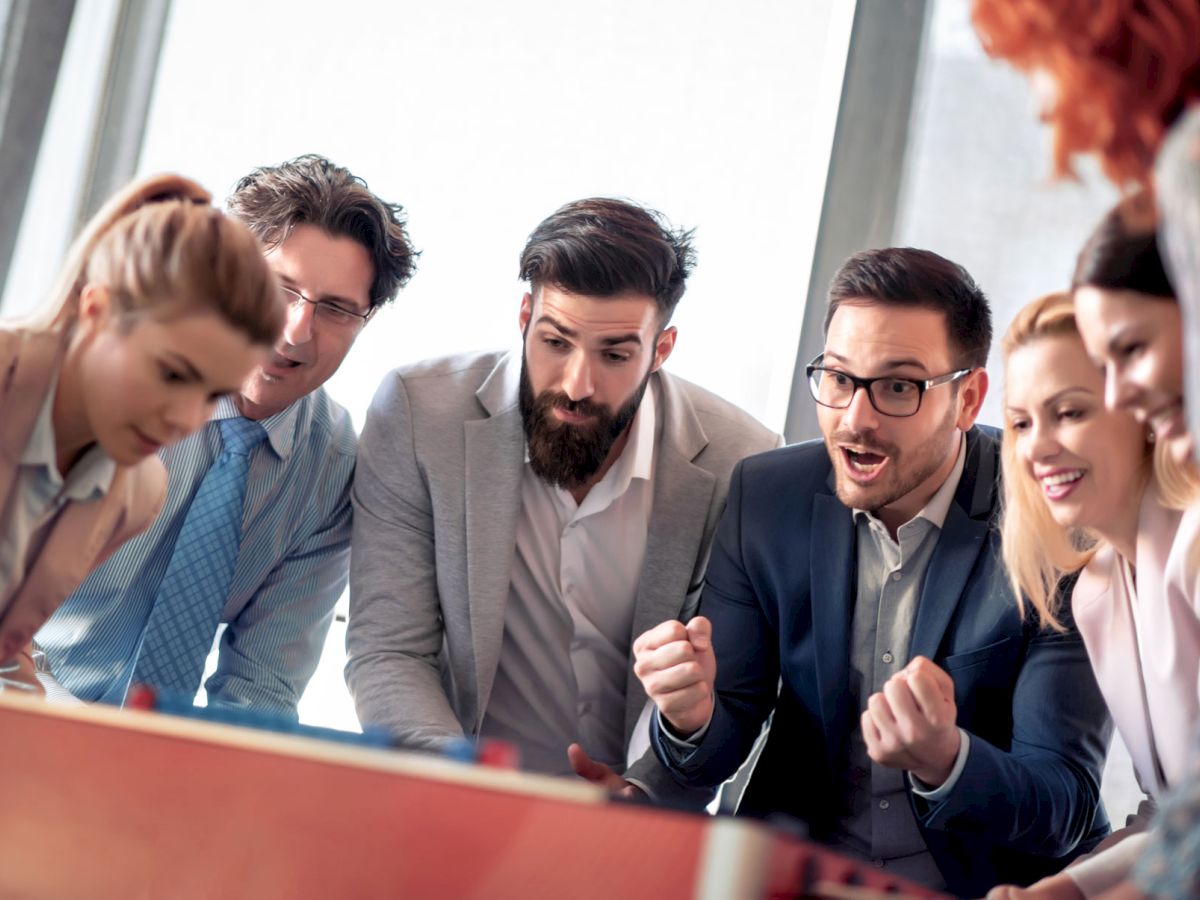 A group of people in business attire are excitedly gathered around a table, appearing engaged and enthusiastic about something they're viewing.