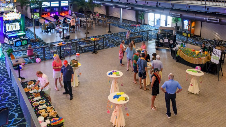 A group of people is attending a social event in a large room with games, decorations, and food tables.